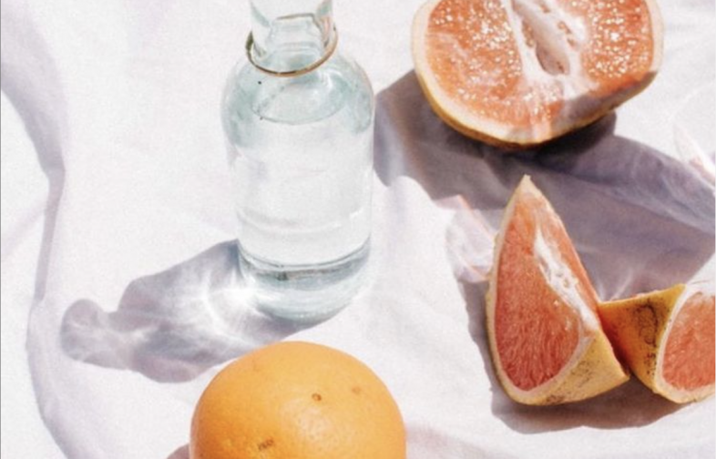Glass bottle with water surrounded by whole and cut citrus